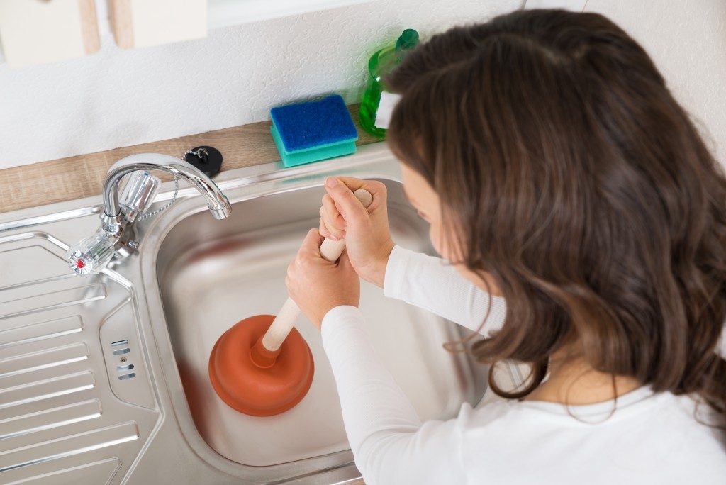 Woman using a plunger to unclog the sink