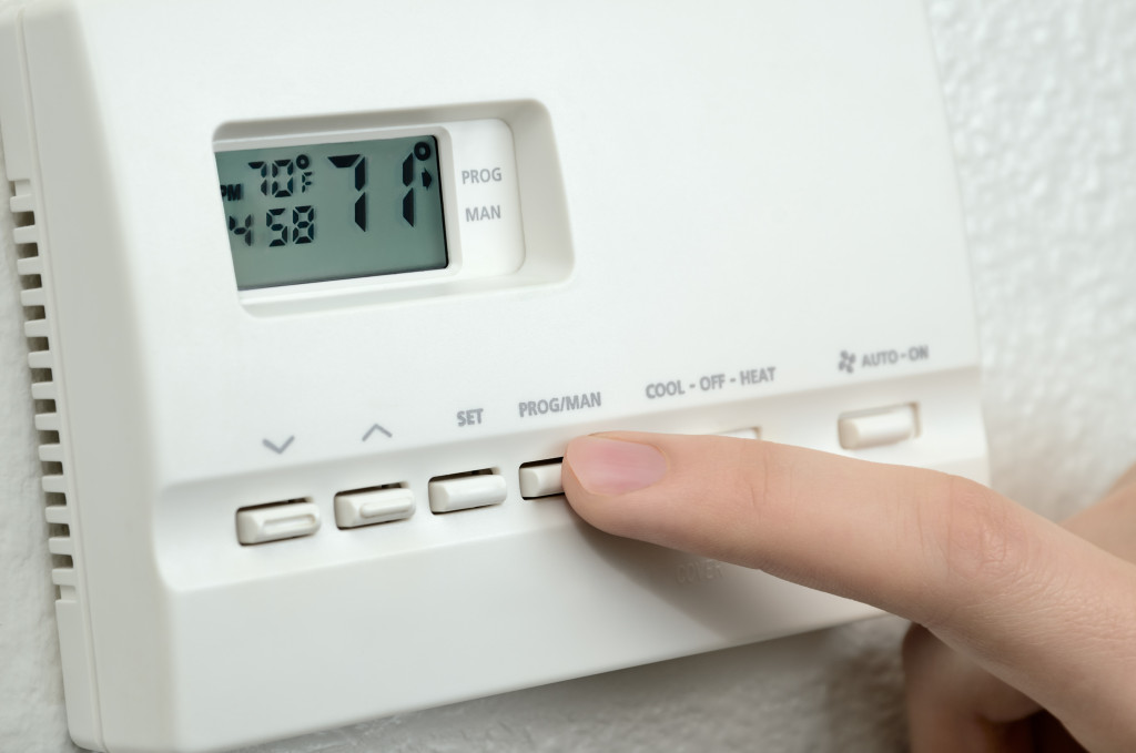 A finger pressing a button on a digital thermostat