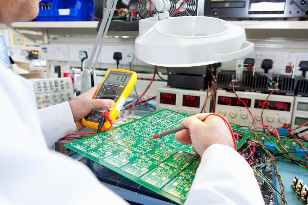 An engineer using a test head while examining a circuit board under a magnifying lamp