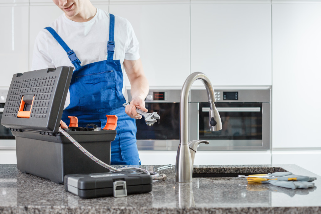 A professional holding tools for fixing the plumbing under the kitchen sink