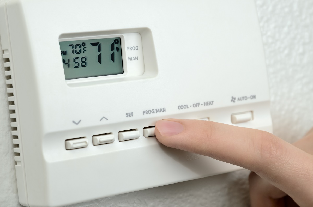 A hand setting the temperature on a thermostat